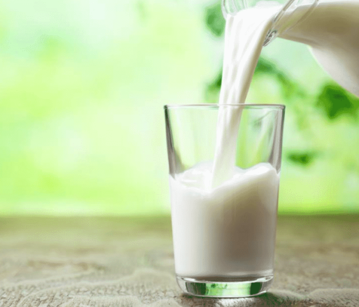 fresh milk from a jug is poured into a glass