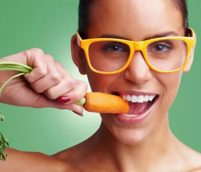 a woman with yellow glasses eats a carrot