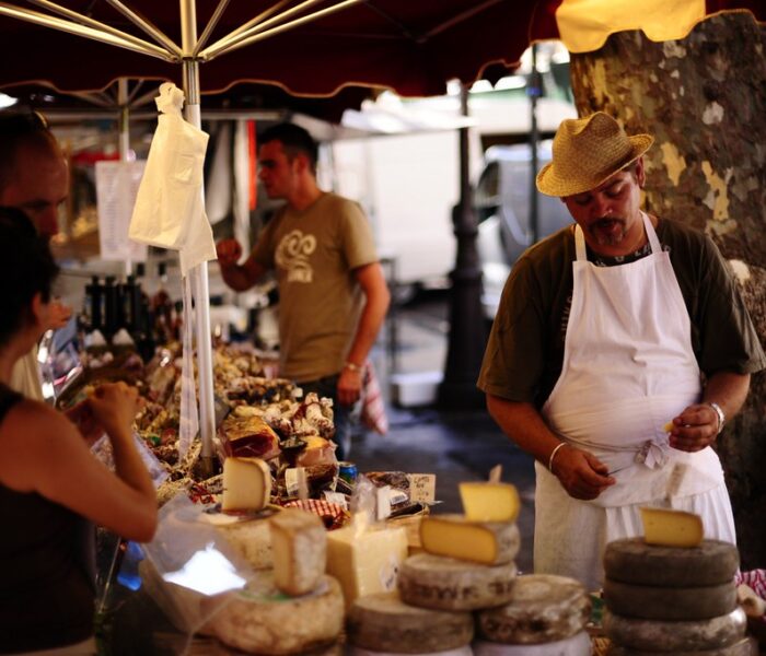 a man and a woman are in a market where they sell cheese